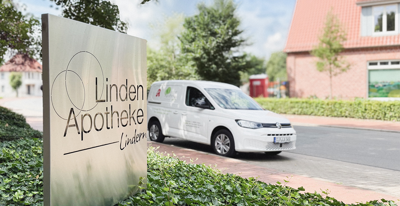 Ein weißer Lieferwagen mit Apotheken-Logo steht vor einer Hecke am Straßenrand. Im Vordergrund ist ein Schild mit der Aufschrift „Linden Apotheke Lindern“ zu sehen.