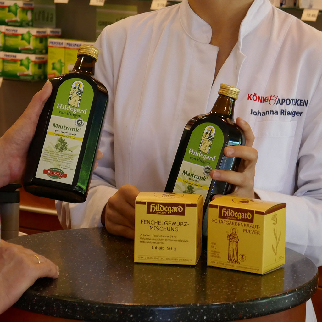 Eine Apothekerin präsentiert Hildegard Produkte: zwei grüne Flaschen und zwei gelbe Schachteln.