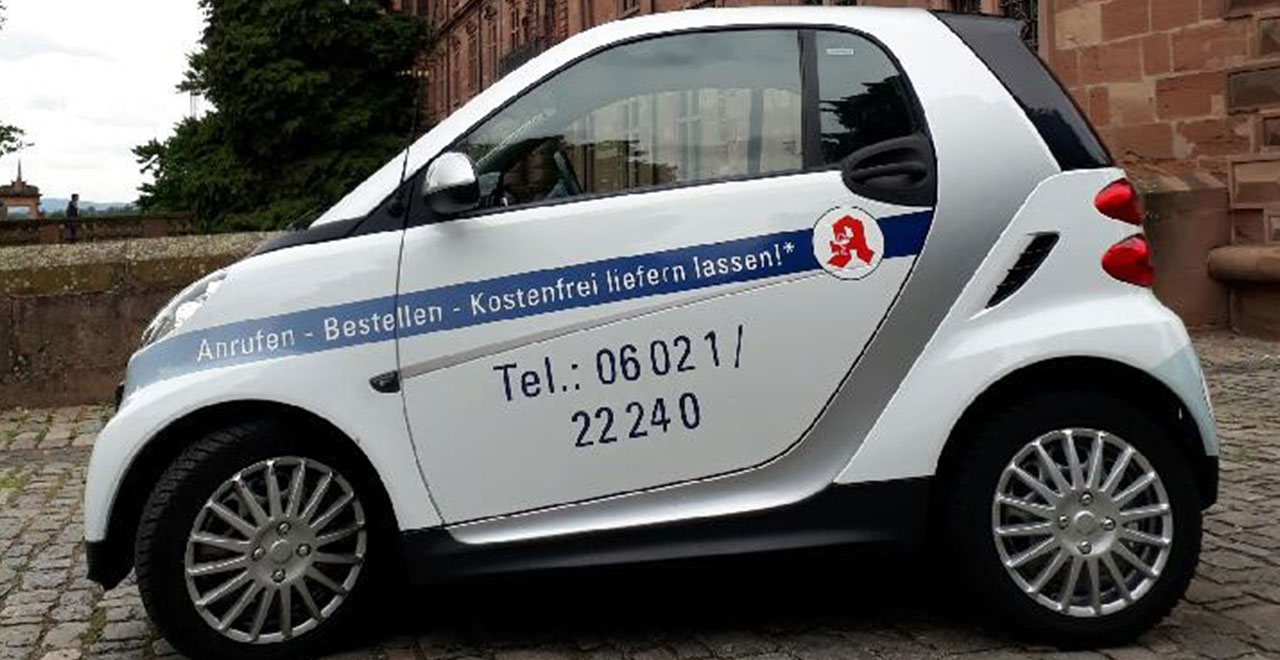 Weißes Botendienstfahrzeug von der Schwanen-Apotheke mit Werbeaufschrift und Telefonnummer.