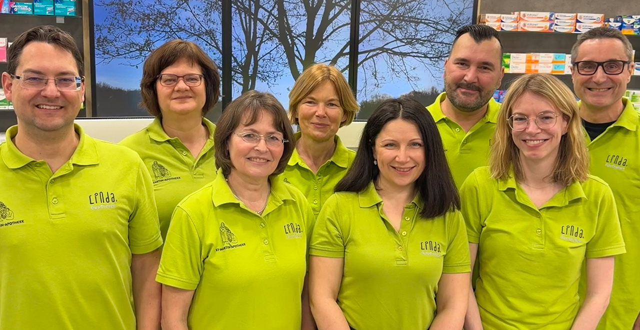 Team der St. Martin Apotheke in grünen Polo-Shirts, lächelnd in der Offizin stehend.