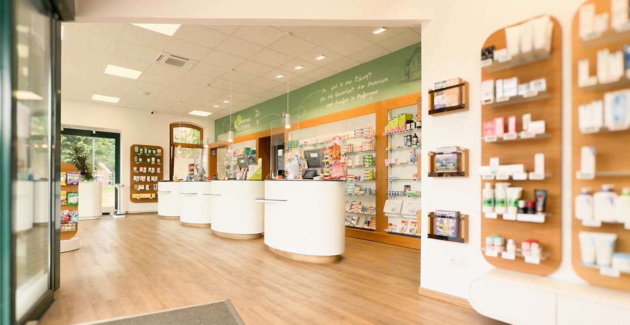 Verkaufsbereich einer Apotheke mit mehreren runden weißen Theken, modernen Kassensystemen und Medikamenten in Regalen hinter Glas.