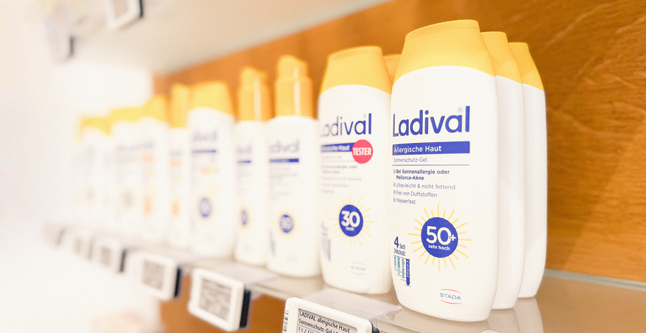 Nahaufnahme von Ladival Sonnenschutz-Gel für allergische Haut in weißen Flaschen mit gelben Deckeln, sortiert in einem Apothekenregal.