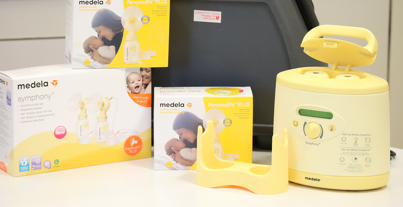 Mehrere Medela-Produkte zur Milchpumpenvermietung, darunter Kartons und eine gelbe elektrische Milchpumpe vom Typ „Symphony“. Die Verpackungen zeigen eine stillende Mutter mit Baby.