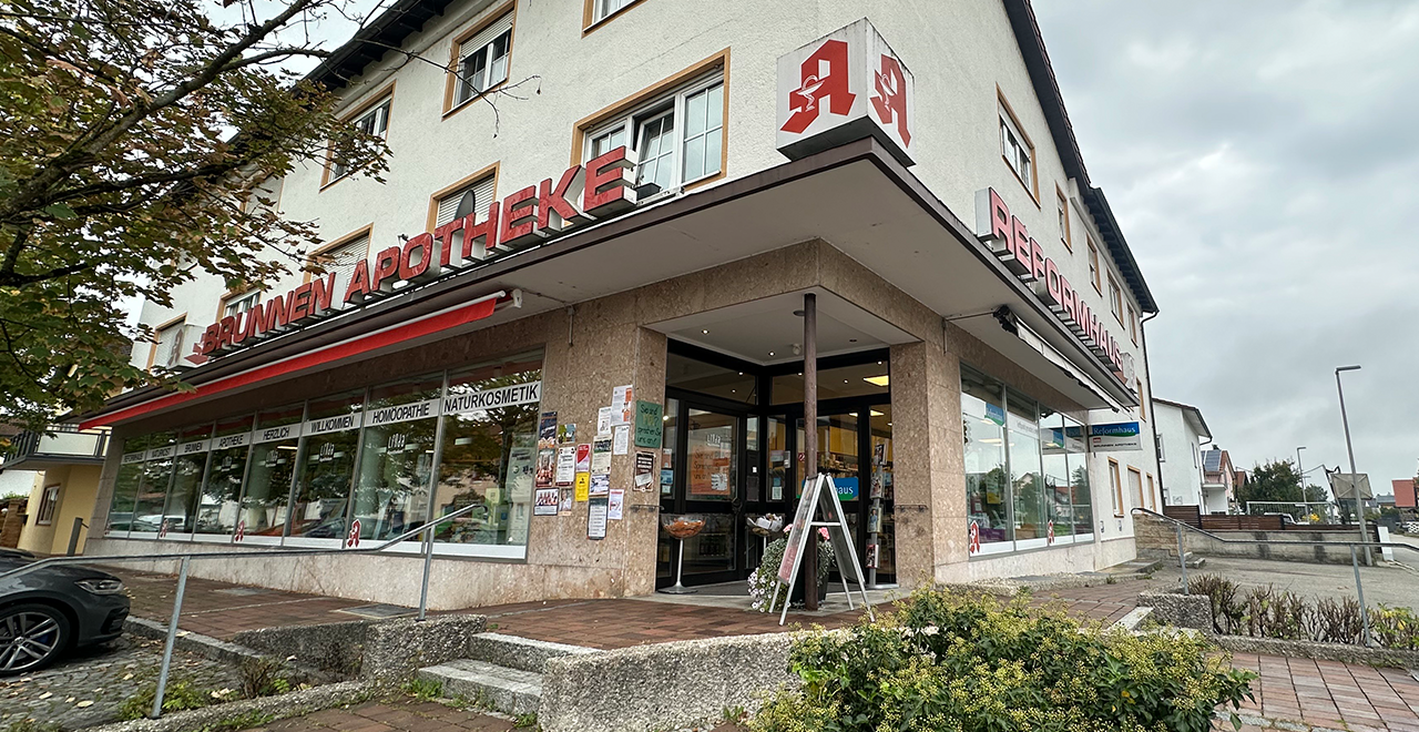 Seitenansicht des Reformhauses und der Brunnen Apotheke in einem mehrstöckigen Gebäude mit großen Fenstern und Werbeschildern.