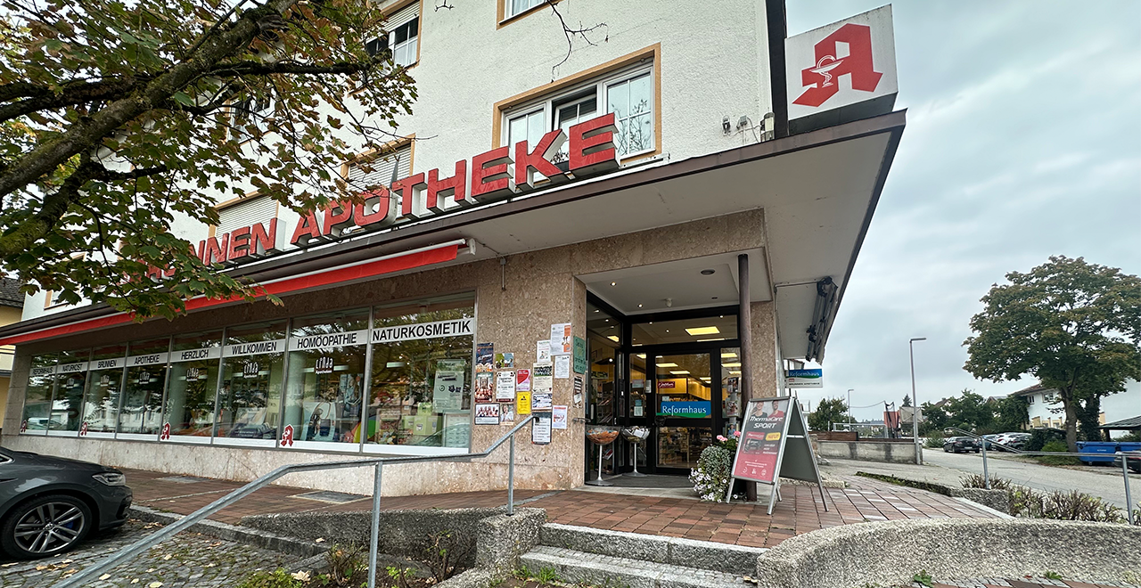 Eingang einer Apotheke mit Reformhaus in einem Eckgebäude, barrierefreier Zugang über Rampe, große Fenster mit Beschriftung zur Naturkosmetik und Homöopathie.