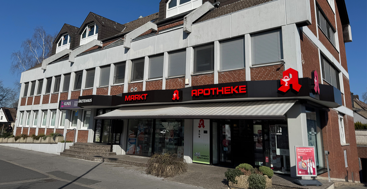 Außenansicht einer Apotheke in einem mehrstöckigen Gebäude mit dem beleuchteten Schriftzug „Markt Apotheke“ über dem Eingang.