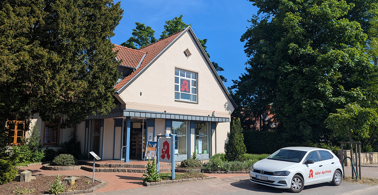 Ein charmantes Gebäude mit einem hellen, einladenden Aussehen und einer klaren Beschilderung. Direkt vor dem Gebäude steht ein Auto mit dem Apothekenlogo.