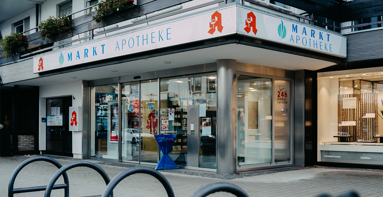 Außenansicht der „Markt Apotheke“ mit Glasfront und 24h-Abholsystem am Eingang.