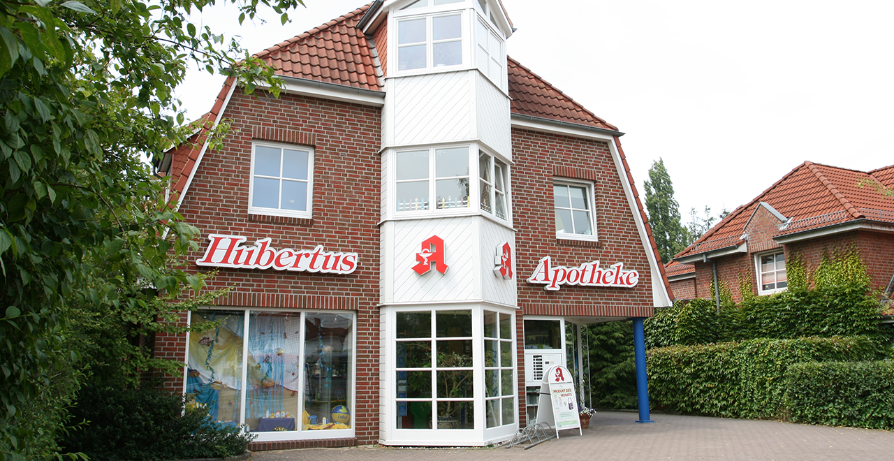 Fassade der Hubertus-Apotheke mit roten Ziegeln, weißem Erker und Apotheken-Schriftzug.
