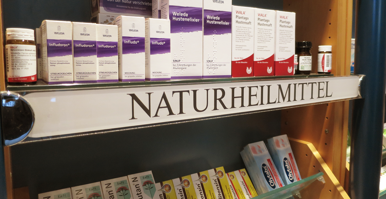 Apothekenregal mit Naturheilmitteln und dem Schild ‚Naturheilmittel‘.