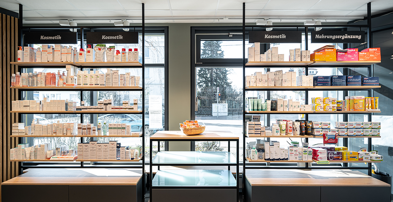 Nahaufnahme des Verkaufsbereichs in der Park-Apotheke. Im Vordergrund sind Kassenplätze sichtbar, mit Bildschirmen für die Kundenberatung und Regalen im Hintergrund, die eine Vielzahl von Medikamenten und Gesundheitsprodukten zeigen. Das Logo „Park-Apotheke“ ist ebenfalls an der Wand hinter den Regalen angebracht.