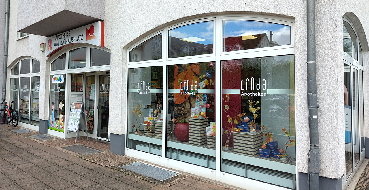 Außenansicht der Apotheke. Die große Glasfassade zeigt den Eingang mit dem Logo der Apotheke 