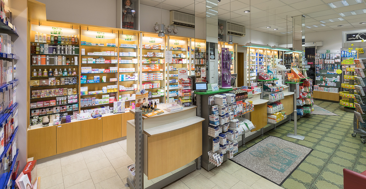 Innenaufnahme der Hanauerland Apotheke. Im Vordergrund sind Regale mit Gesundheitsprodukten und Arzneimitteln zu sehen. Der Empfangstresen ist gut beleuchtet, mit mehreren Produkten auf Ausstellungsflächen. Der Raum ist ordentlich und gut organisiert.