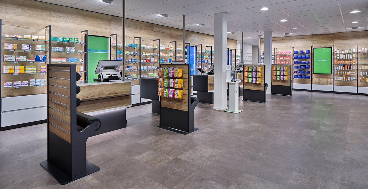 Modern eingerichteter Verkaufsraum einer Apotheke mit Regalen voller Medikamente und mehreren Beratungsplätzen.