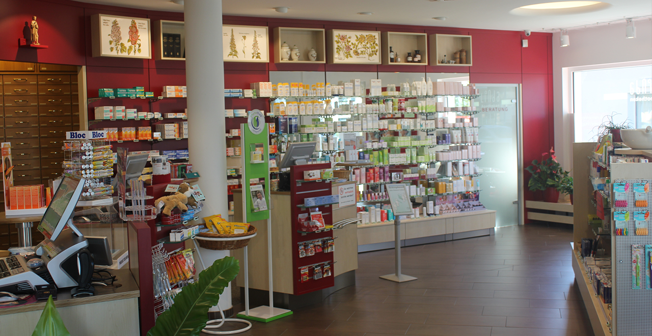 Heller Verkaufsraum der Apotheke mit Regalen voller Pflegeprodukte, Beratungstheke und digitalem Kassensystem.
