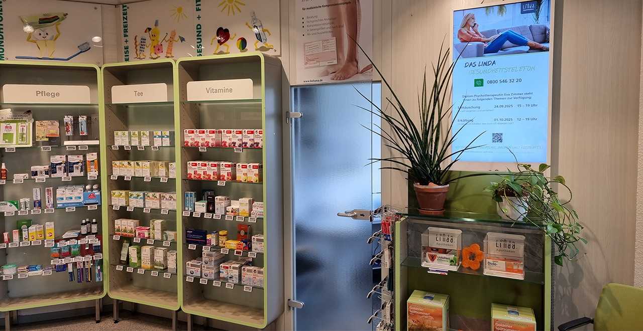 In dieser Apotheke ist ein gut organisierter Verkaufsbereich zu sehen, der Produkte wie Pflegeartikel, Tees und Vitamine umfasst. Es gibt bunte, kinderfreundliche Illustrationen an der Wand, die gesunde Lebensweise und Freizeitaktivitäten darstellen. Ein Monitor zeigt Gesundheitsinformationen und Details zu Veranstaltungen.