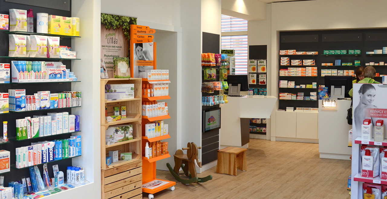 Innenansicht einer modernen Apotheke mit Regalen voller Produkte, Beratungsbereich und Verkaufsfläche.