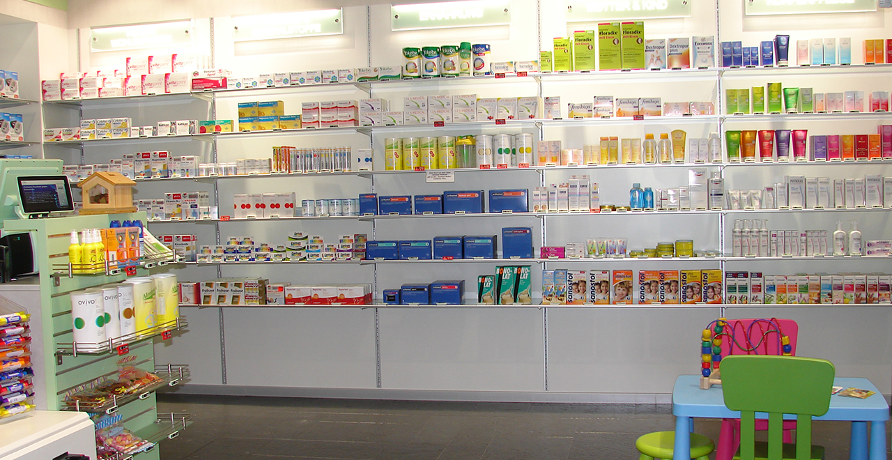 Verkaufsbereich einer Linda-Apotheke mit klar strukturierten Regalen für Arzneimittel und Pflegeprodukte. Rechts im Bild befindet sich eine kleine Spielecke mit bunten Kindermöbeln.