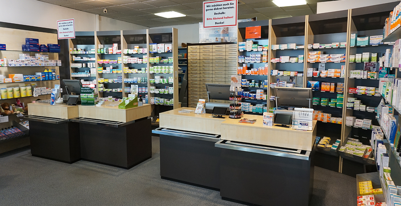 Frontalansicht der Löwen Apotheke in einem mehrstöckigen Gebäude mit großen Fenstern. Oberhalb des „apotheke“-Schriftzugs ist ein beleuchtetes Zahn-Symbol zu sehen. Das Gebäude hat ein dunkles Dach mit mehreren Gaubenfenstern.