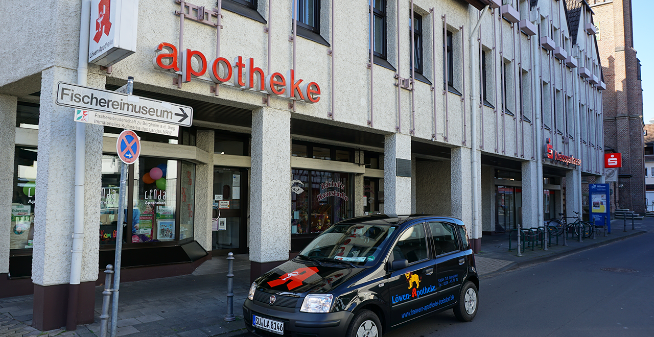 Innenansicht der Apotheke mit drei modernen Verkaufstresen. Dahinter befinden sich hohe Regale mit zahlreichen Medikamenten, Gesundheitsprodukten und Kosmetikartikeln. In der Mitte hängt ein Schild mit der Bitte, Abstand zu halten. Die Atmosphäre ist sauber und ordentlich.