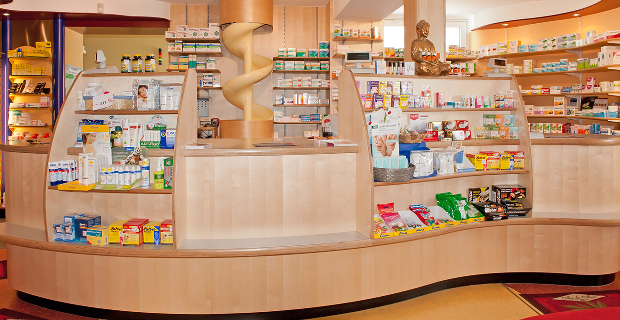 Moderne Verkaufstheke der St. Alto Apotheke mit Arzneimitteln, Gesundheitsprodukten und einer dekorativen Wendeltreppe im Hintergrund.