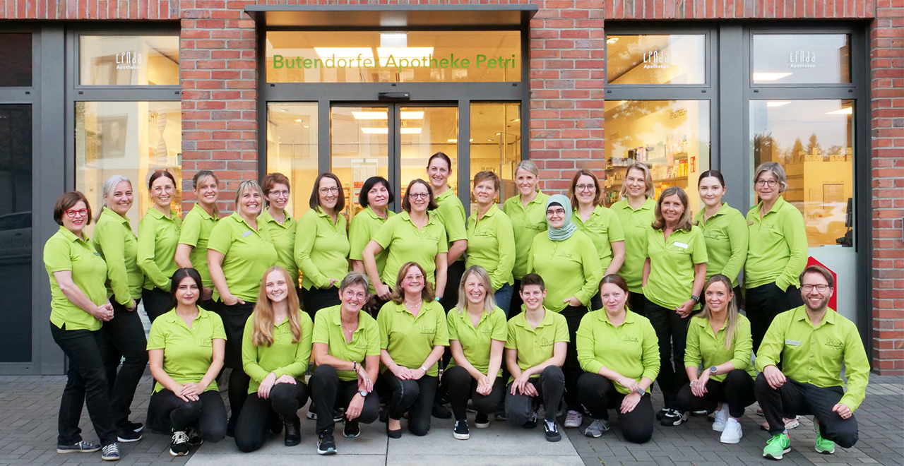 Gruppenfoto des Apothekenteams in grünen Oberteilen vor dem Eingang der „Butendorfer Apotheke Petri“.